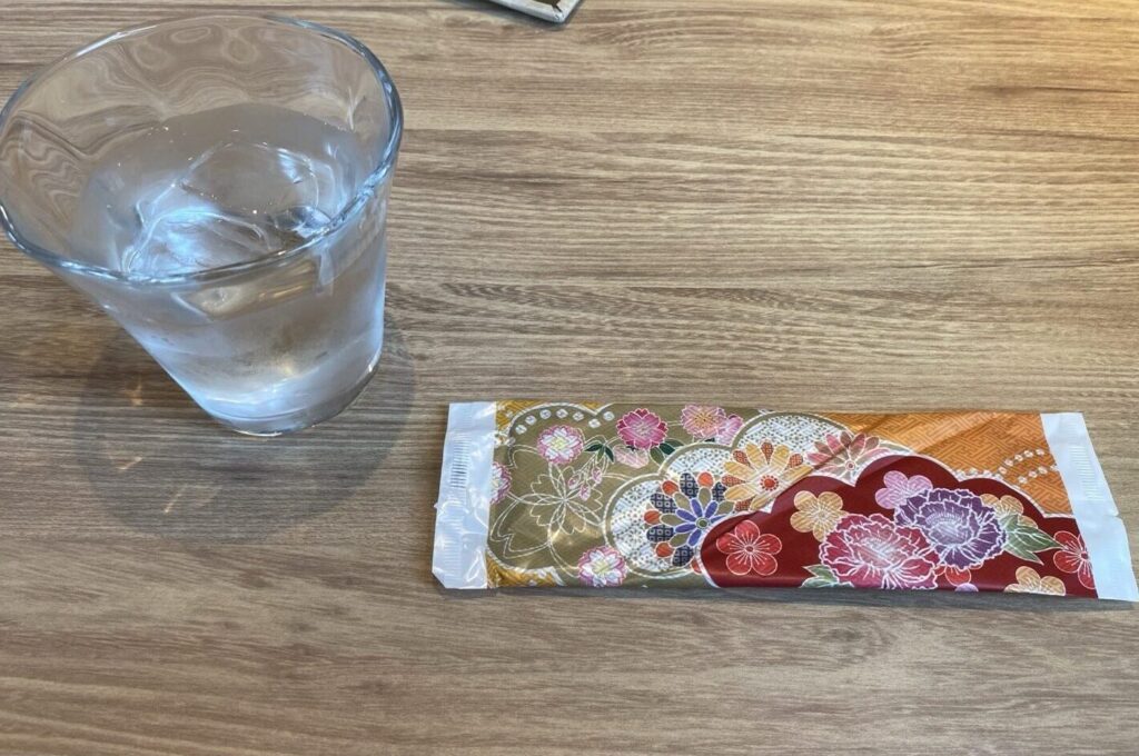 和柄の袋に入ったおしぼりと氷入りのお冷のグラス