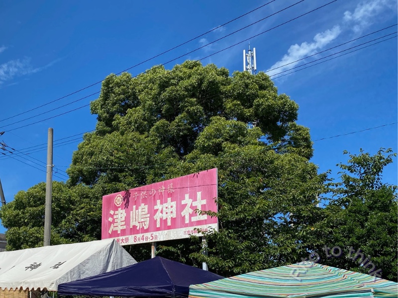 夏季大祭の日程が書かれた津嶋神社の看板と青空