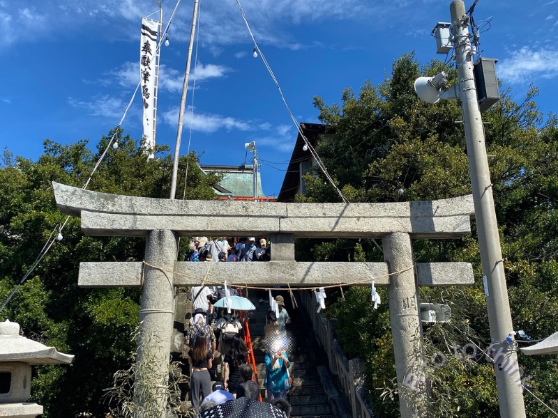 津嶋神社の本殿へ続く石の鳥居と石段を上る参拝者