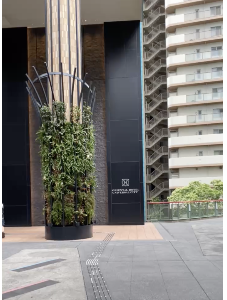 植物に囲まれた柱と、「ORIENTAL HOTEL UNIVERSAL CITY」のロゴがある黒い壁のホテル入口
