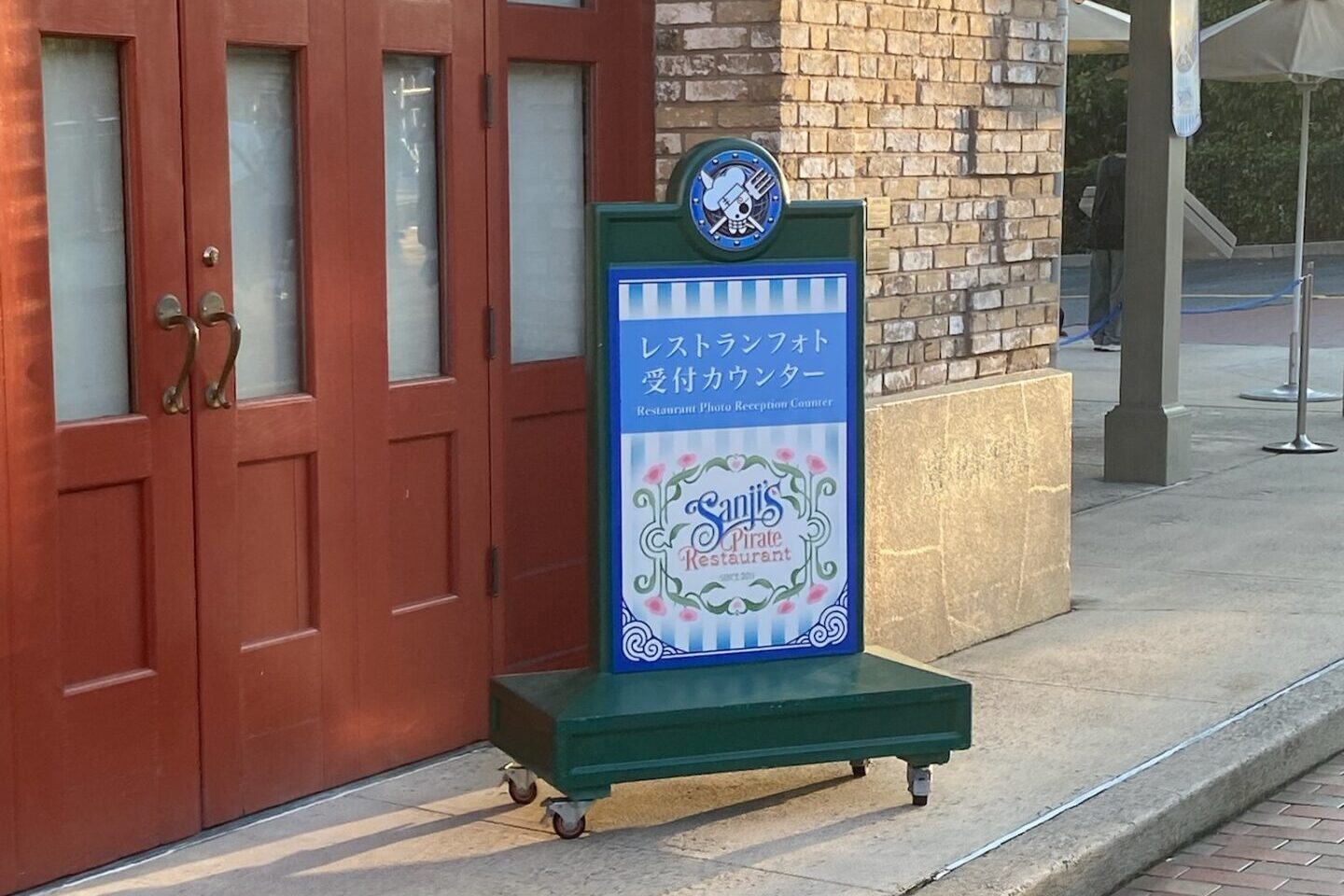 赤い扉の横に置かれた「レストランフォト受付カウンター」とSanji's Pirate Restaurantのロゴが入った看板