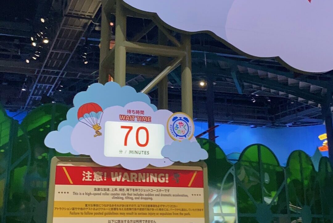 雲の形の看板に「待ち時間 WAIT TIME 70分」と「よやくのり」のマークが表示された、スヌーピーのフライング・エース・アドベンチャーの入口