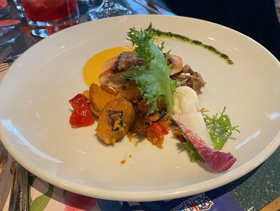 白い皿に盛られた魚料理。葉野菜と焼き野菜、黄色いソースが添えられている