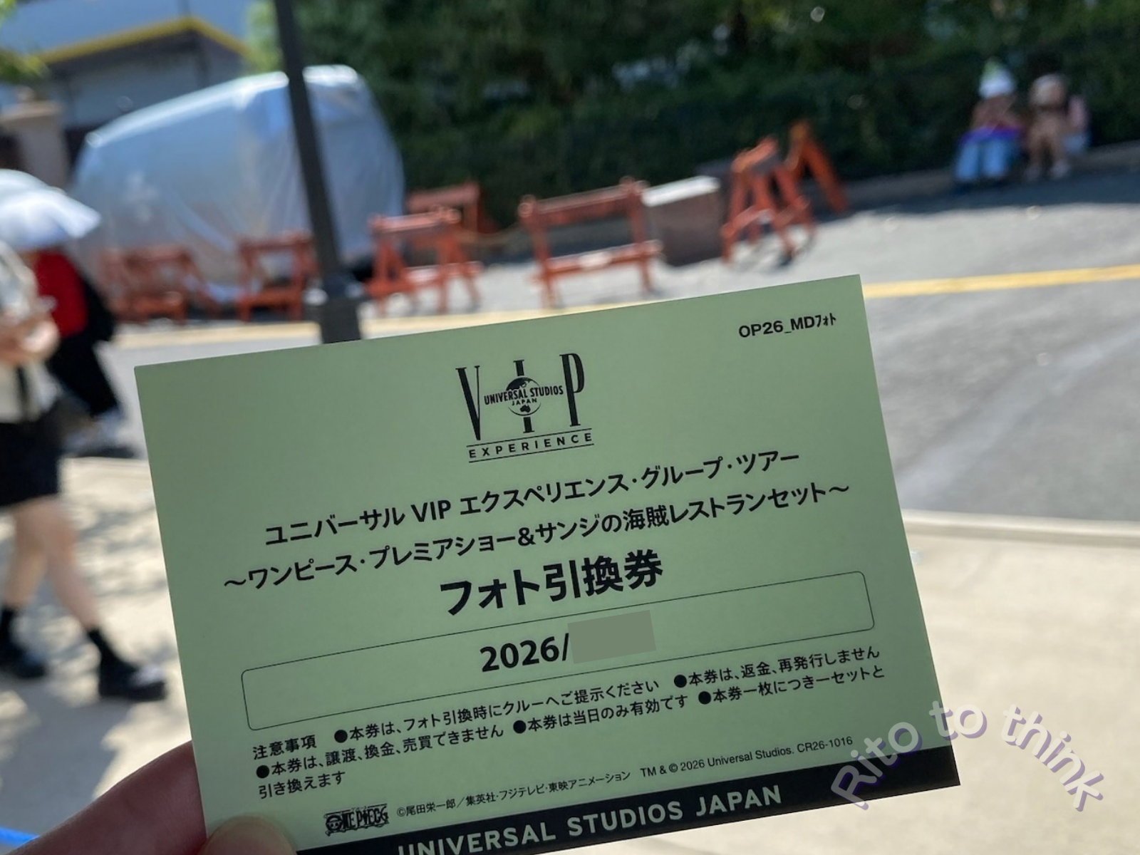 2026年のユニバーサルVIPエクスペリエンス・グループ・ツアーの「フォト引換券」を、パークの通りで手に持っている
